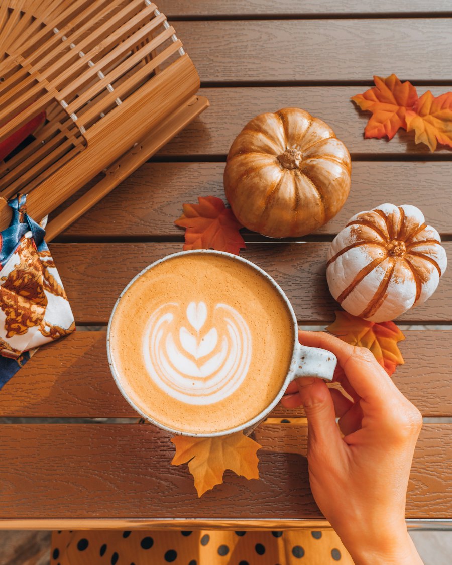 A latte with leaf art beside small pumpkins and autumn leaves